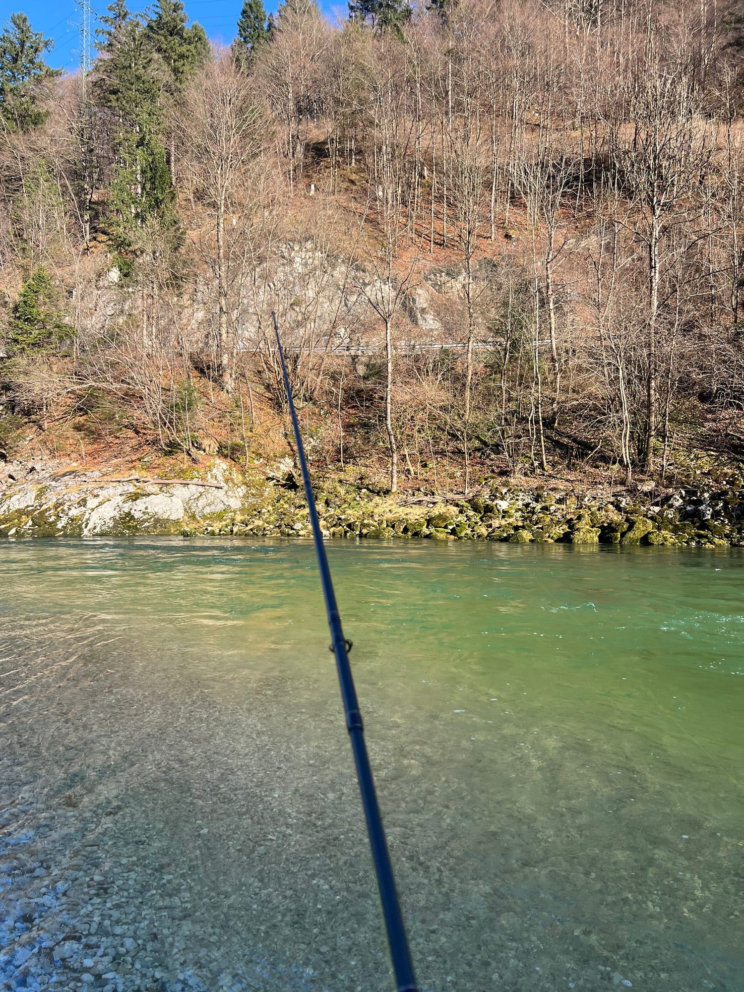 A fly rod held out over clear green water from a rocky bank