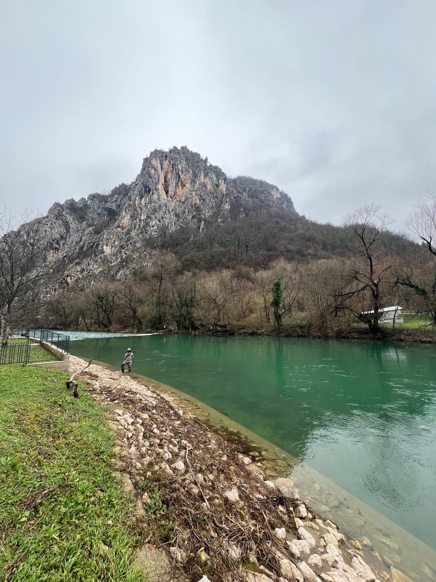 An angler on the riverside path below a rocky bluff