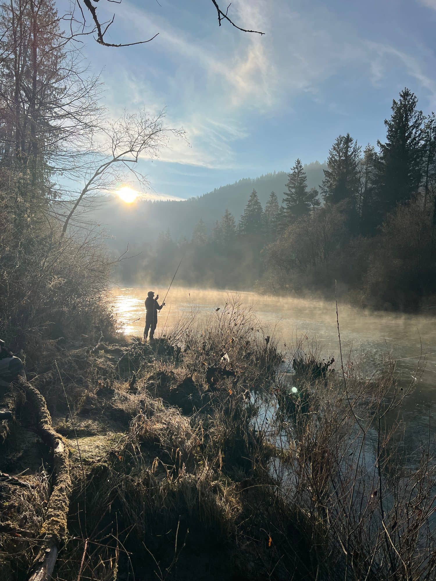 An angler casting into steam rising off the river at first light