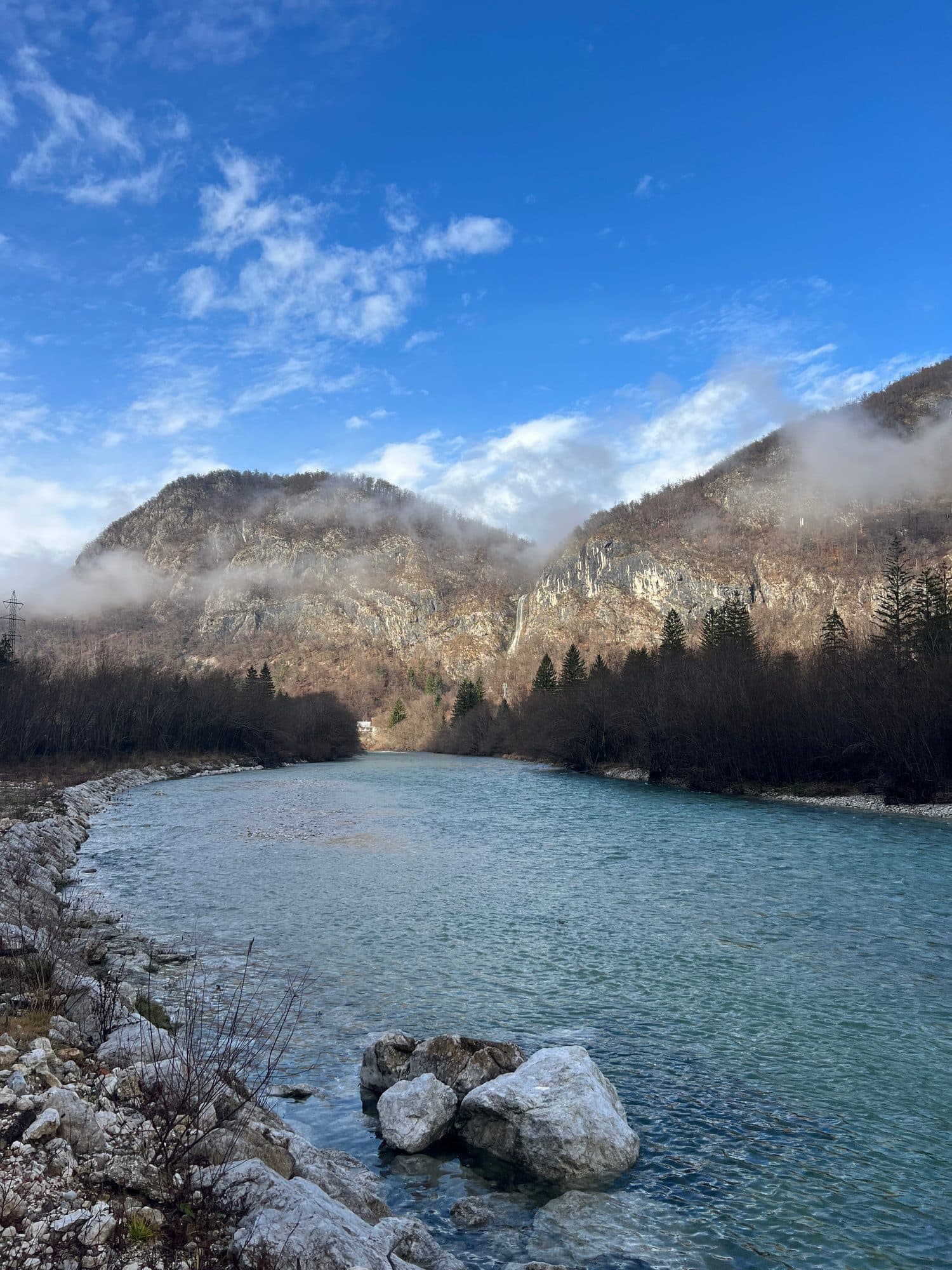 A river bend below a cloud-capped ridge, framed by bare winter trees