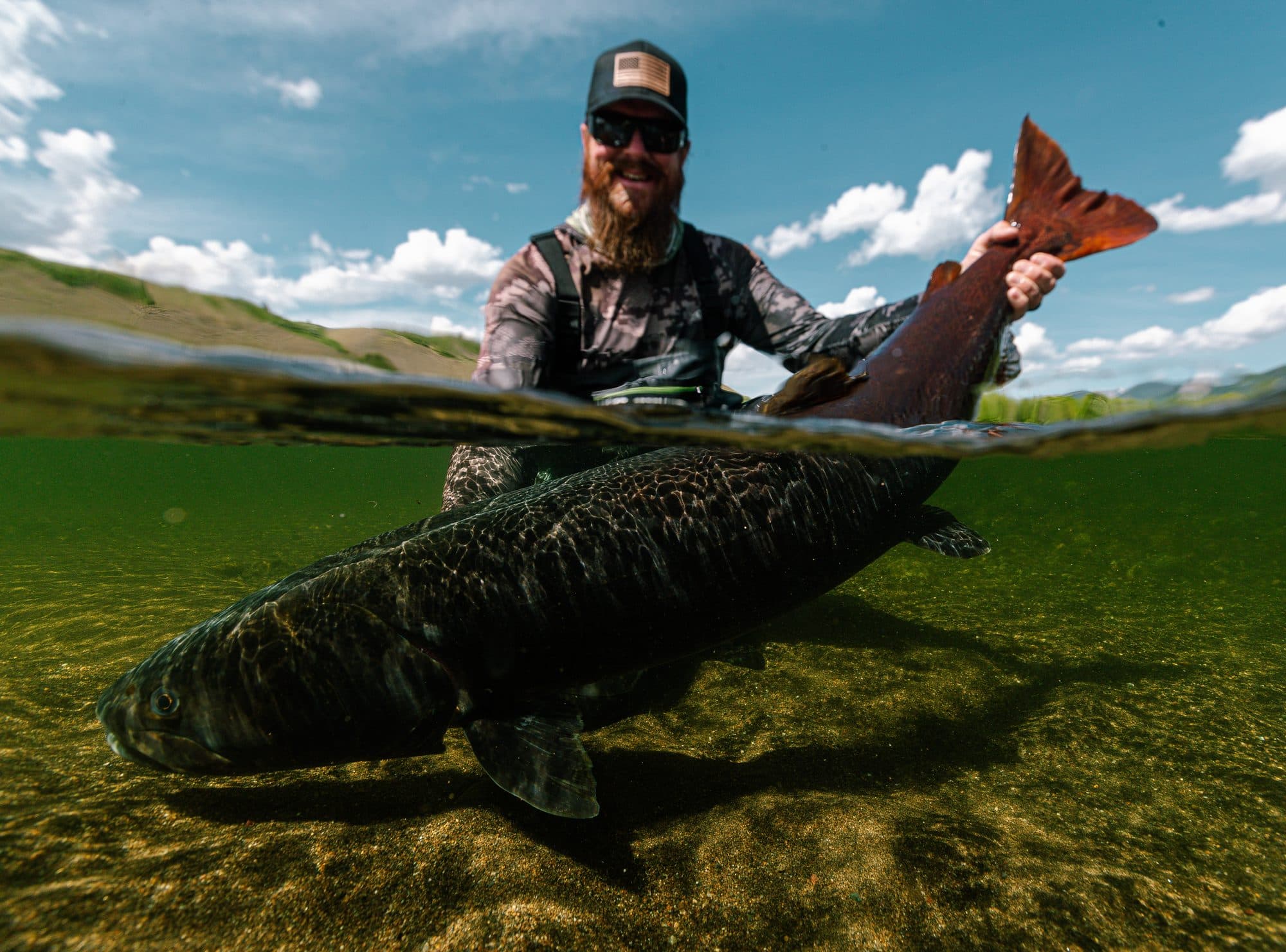 Angler kneeling on a remote gravel bar with a taimen