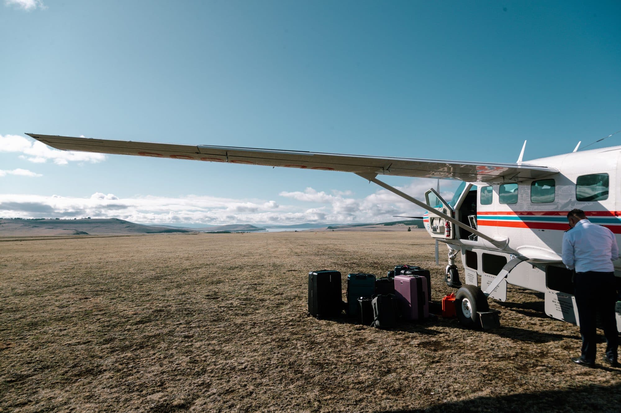 Bush plane parked on a remote gravel airstrip, expedition gear beside it