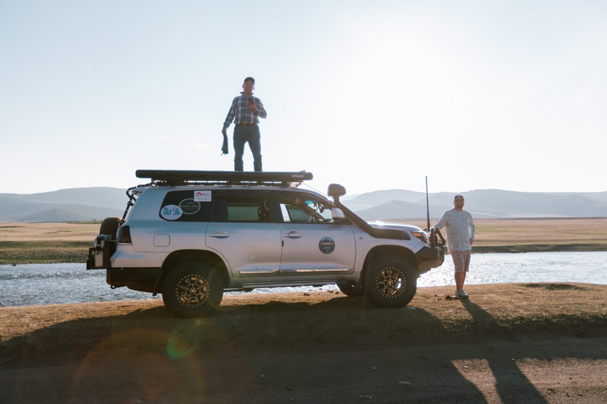 Guide standing on a vehicle roof scanning the river at sunset