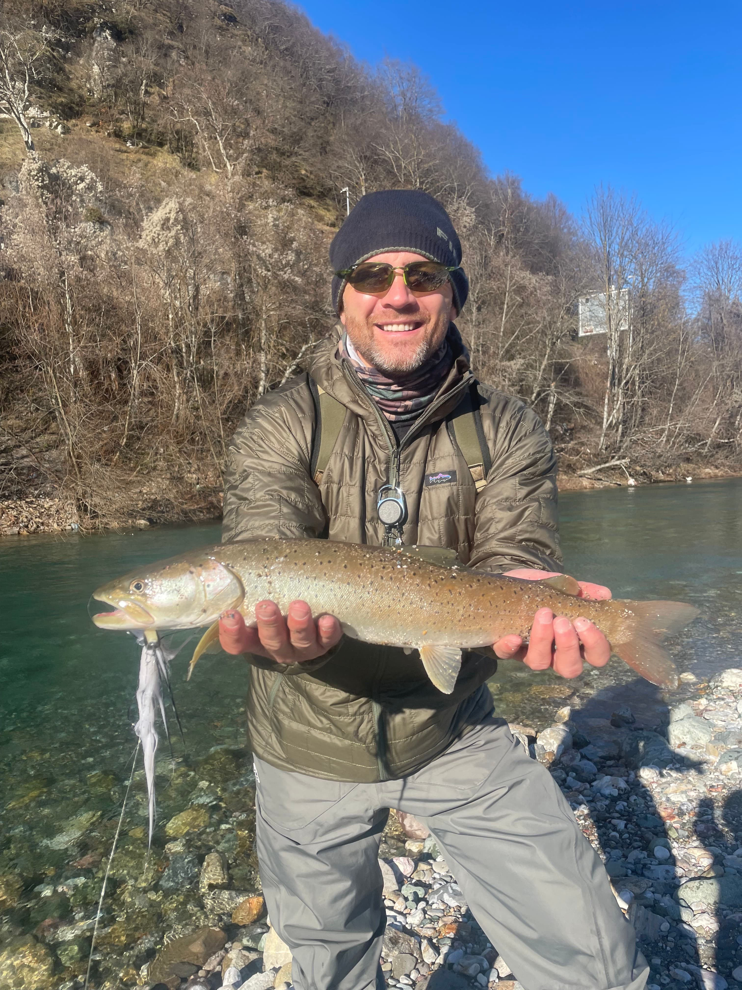 A smiling angler holding a huchen above the water on a bright winter day